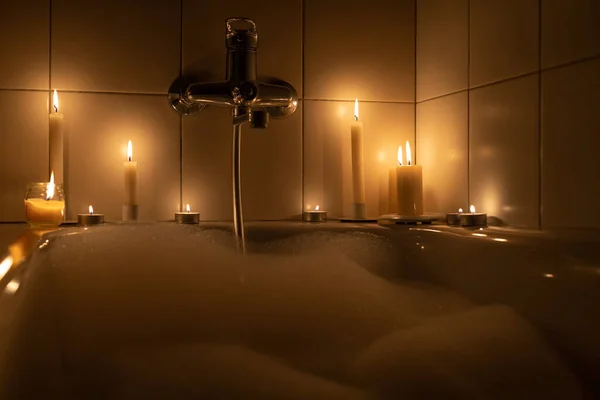 Karanlıkta mum ışığında beyaz köpüklü romantik bir banyo.