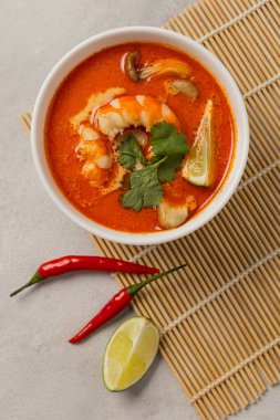 Beyaz kase taze Tom Yum çorbası bambu tezgahında hafif arka planda malzemelerle