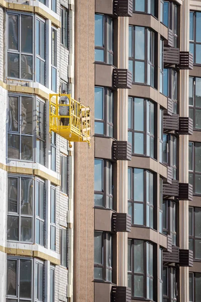 Real estate market. Scaffolding at height. Construction works. Residential building. Modern residential complex. Exterior works. Yellow scaffolding with builders at height.
