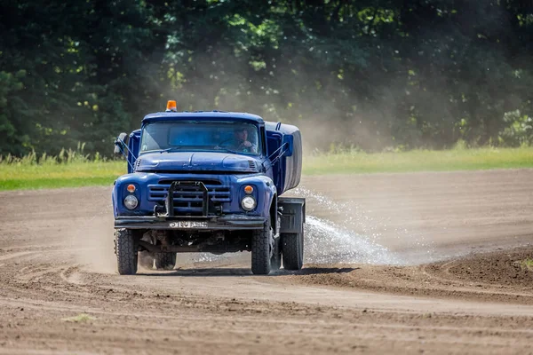 The truck waters the track at the racetrack for horse racing. Agricultural transport. Water truck. Preparation of the track at the racetrack. Spraying the ground with water.