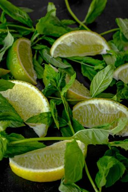 Siyah arka planda limon dilimleri ve nane filizi. Limon ve nane. Yaz tazeliği. Doğal arka plan. Limonata malzemesi. Durgun yaşamda sarı ve yeşil renkler. Bir tutam nane. Dilimlenmiş limon.