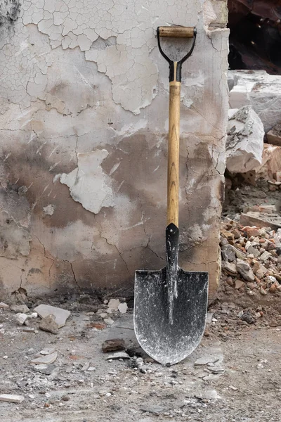 A shovel on the background of a shabby wall of an old house. Shovel at construction site. Garden and construction tools. Item for digging.