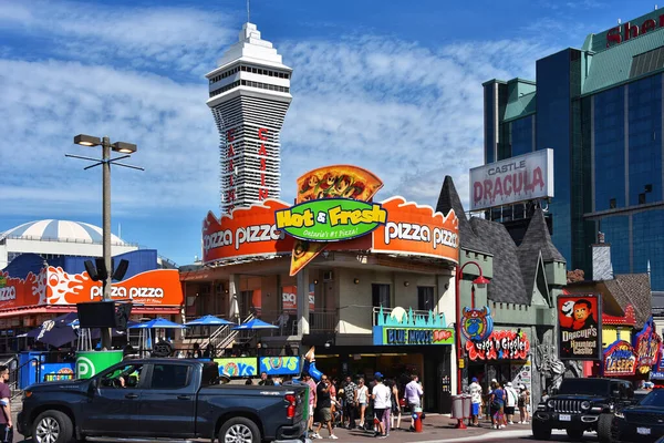 Niagara Falls, Canada  August 13, 2022 Pizza Pizza restaurant and various tourist attractions on the busy street Clifton Hill. Casino Niagara tower can be seen in the background.