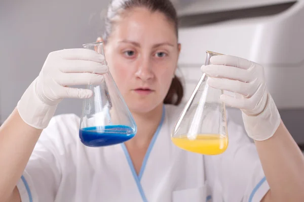 Mulher examinar garrafas coloridas encher com produtos químicos — Fotografia de Stock