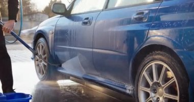 Yüksek basınçlı su ile anonim kişi tarafından yıkanan modern bir araca yakın çekim. Çok kirli bir araba temiz suyla temizlenir.