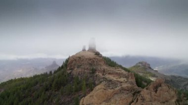 Sisli bir günde dağın tepesindeki büyük bir kayanın insansız hava aracı uçuşu, Roque Nublo, Pico de Las Nieves, Gran Canaria