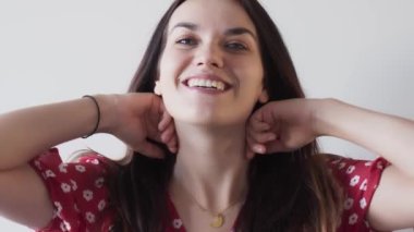 Kırmızı elbiseli mutlu güzel kız beyaz arka planda yalıtılmış saçları dalgalanıyor. Kadın uzun saçlı. Yavaş çekim görüntüleri.