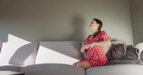 Attraktiv Ung Kvinna Röd Klänning Vilar Grå Soffa Och Stretching — Stockvideo