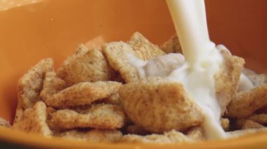 Mısır tarçınlı gevreğin içine süt dökülüyor. Yavaş çekimde sıçrıyor. Turuncu arka planda sağlıklı kahvaltı..