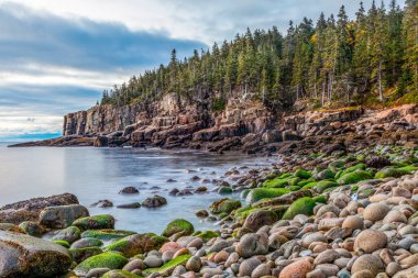 Güneş doğmadan hemen önce parlayan ışık, Boulder Sahili 'ndeki yuvarlak taşları ve Acadia Ulusal Parkı' ndaki Acadia Kayalıkları 'nın dik kaya duvarlarını aydınlatıyor. Issız Ada, Maine.