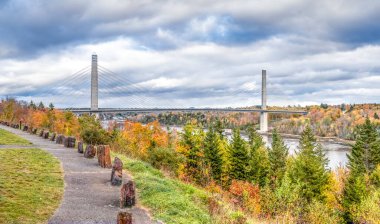 Penobscot Narrows Köprüsü, bulutlu bir sonbahar gününde Maine, Bucksport yakınlarındaki Penobscot Nehri 'ni çevreleyen renkli yapraklarla çevrilidir..