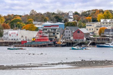 Doğu Maine 'de bir kasaba topluluğu olan Belfast limanında büyük bir kırmızı römorkör ve birkaç küçük geminin yanı sıra sonbahar yapraklı köy işletmeleri, kiliseler ve ağaçlar görülüyor..