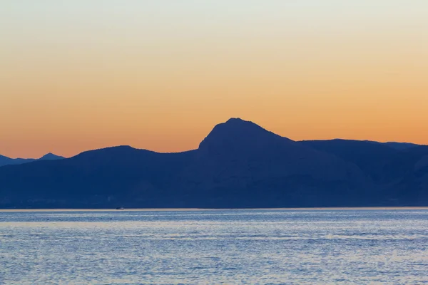 Akşam deniz üzerinde dağ silueti — Stok fotoğraf