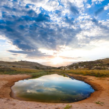 Gün batımında kumlu tepelerin arasında küçük bir göl