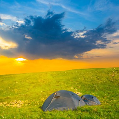 Günbatımında yeşil tepelerin arasında turistik çadır, doğal seyahat kamp sahnesi.