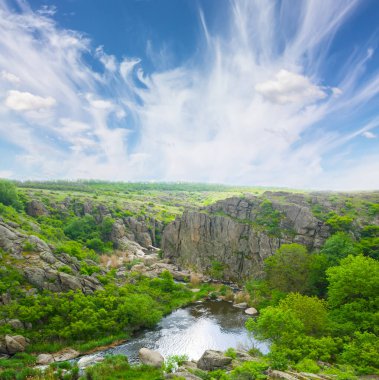 Yeşil çayırlar arasında taşlı kanyondan akan nehir.