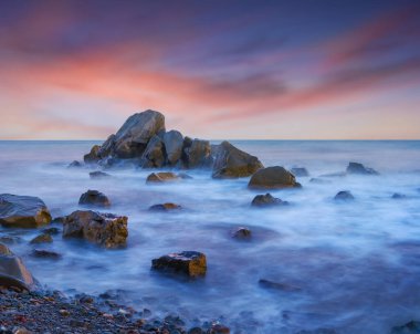 Sabahın erken saatlerinde uzun pozlama sahnesinde taşlarla dolu sessiz deniz kıyıları.