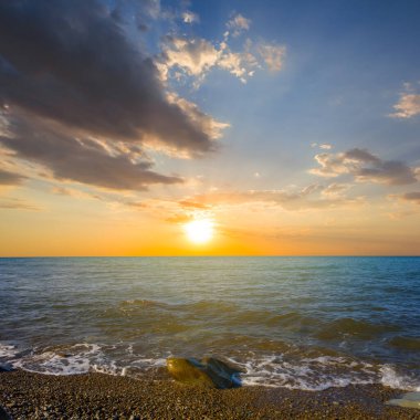 Dramatik günbatımında, yaz deniz sahnesinde sessiz, taştan bir sahil.