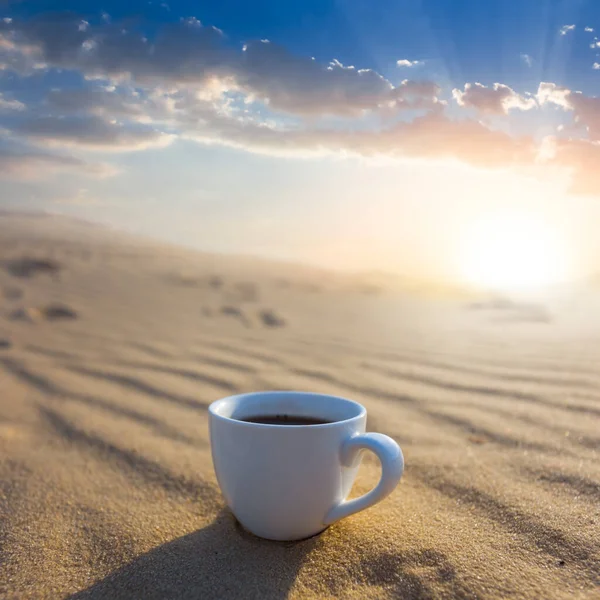 closeup white coffee cup on sand at dramatic sunset, natural outdoor drink scene