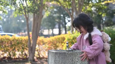 Kız çocuk parkındaki su musluğunda su içiyor.