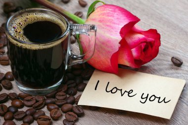 Not: Seni seviyorum. Bir fincan kahve, kavrulmuş kahve çekirdekleri ve ahşap bir masada kırmızı gül. Romantik kahve. seçici odak