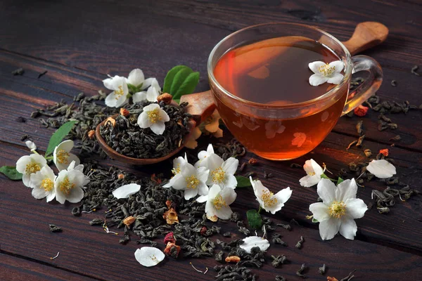 green tea with jasmine. dry green tea leaves with jasmine flowers and a cup of tea on a wooden table.