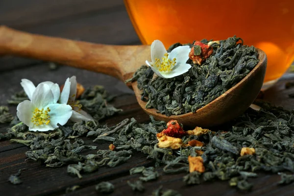绿茶加茉莉花 干绿茶叶子 上面有茉莉花和木勺 桌上有一杯茶 — 图库照片