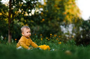 Bebek yaz günü çimlerin üzerinde oturuyor. Moda ve şirin elbiseli çocuk.