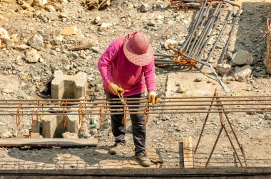 A construction worker equally spread out closed-loop steel bars along the length of deformed bars and ties them together with steel wires.