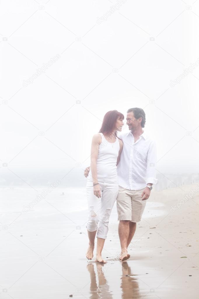 Couple walking on a foggy beach smiling at each other