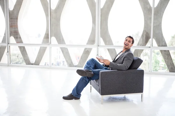 Gut aussehender Mann lacht bei der Arbeit an einem Mini-Denkpad — Stockfoto
