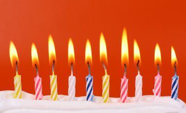 10 lit birthday candles in bright colors with red background clipart