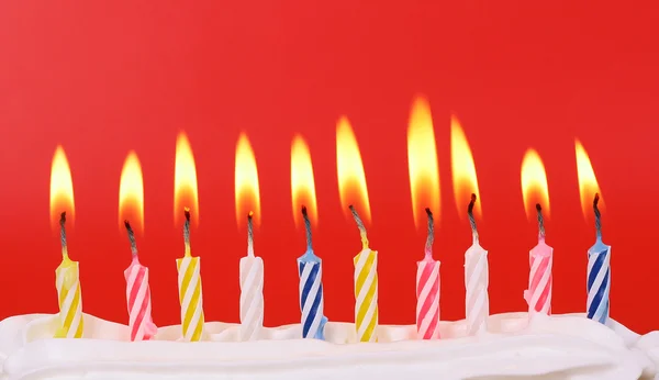 10 velas de aniversário acesas em cores brilhantes com fundo vermelho — Fotografia de Stock