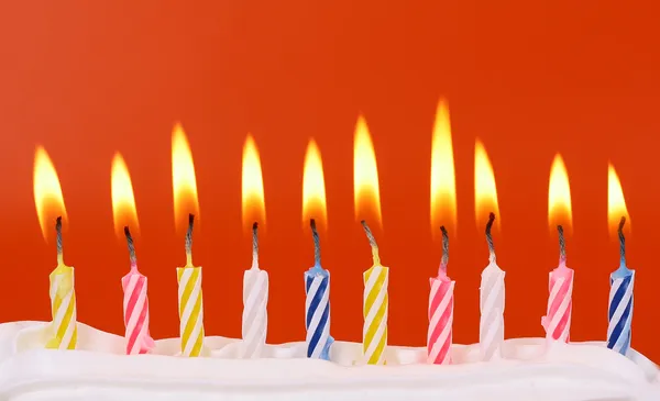 10 velas de cumpleaños encendidas en colores brillantes con fondo rojo — Foto de Stock
