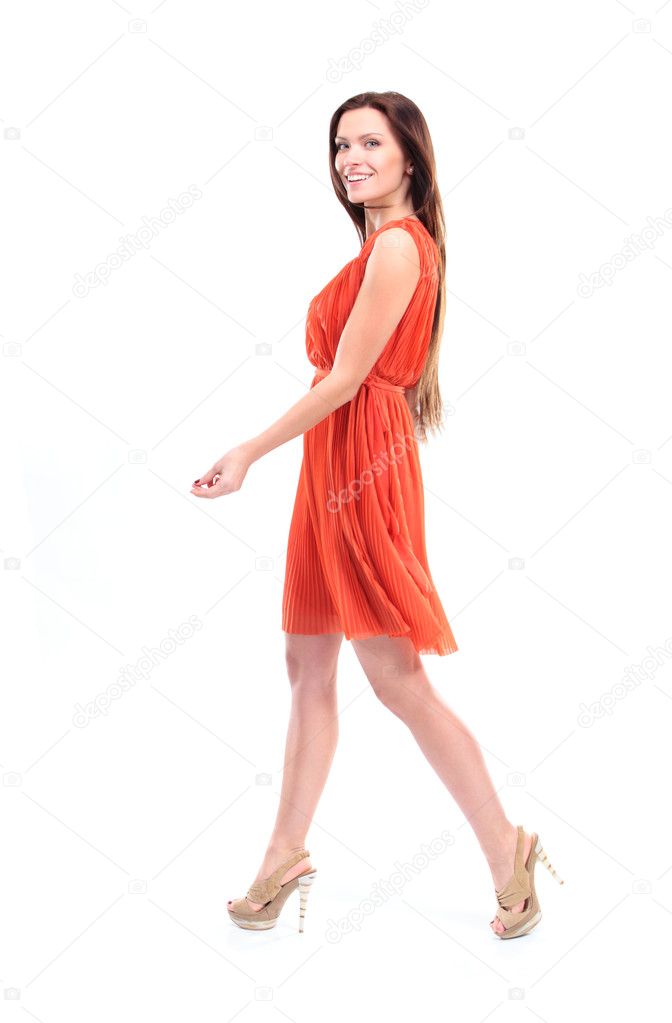 Pretty young female model in dress walking on white background and smiling