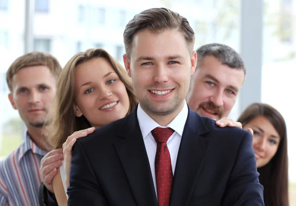 Retrato de um jovem empresário feliz em pé na frente de sua equipe — Fotografia de Stock