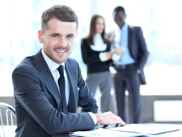 Homem de negócios inteligente feliz com companheiros de equipe discutindo em segundo plano — Fotografia de Stock