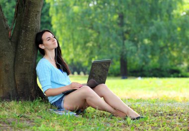 parkta çim üzerinde yalan ve dizüstü kullanan genç kadın