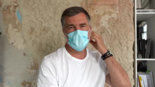 Homem idoso profissional confiante tira máscara médica protetora olhando para a câmera — Vídeo de Stock