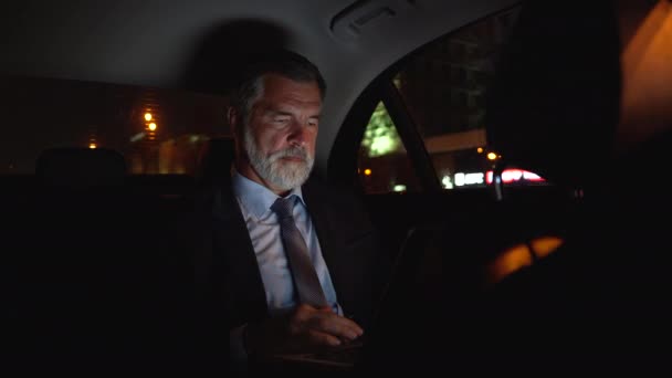 Успішний зрілий бізнесмен в офіційному вбранні, використовуючи ноутбук, сидячи в сучасному автомобілі — стокове відео