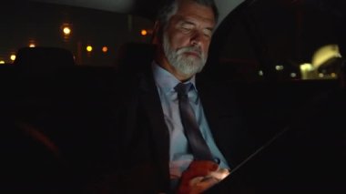 İş arabasında dijital tablet üzerinde çalışan ciddi bir iş adamı.