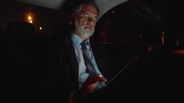 Homme d'affaires mature sérieux travaillant sur tablette numérique dans une voiture de fonction. — Video