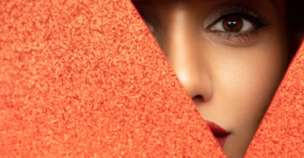 Faccia di una giovane bella ragazza con un trucco luminoso e con paffuto labbra rosse sbircia in un buco in carta rossa lucida. Fotografia Stock