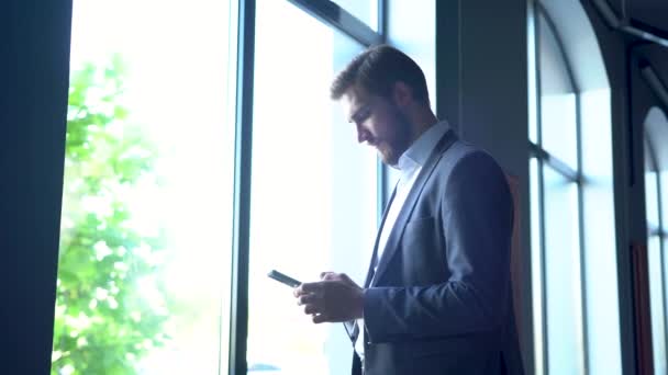 Bonito empresário usando o telefone móvel. Homem jovem mensagens de texto, traindo seu Smartphone enquanto está no escritório — Vídeo de Stock