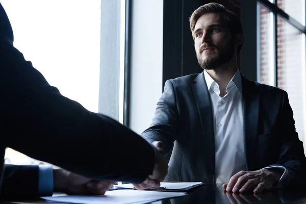 Bra uppgörelse. Två affärsmän skakar hand när de sitter på arbetsplatsen. — Stockfoto