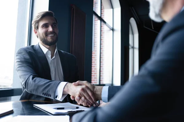 Bra uppgörelse. Två affärsmän skakar hand när de sitter på arbetsplatsen. — Stockfoto