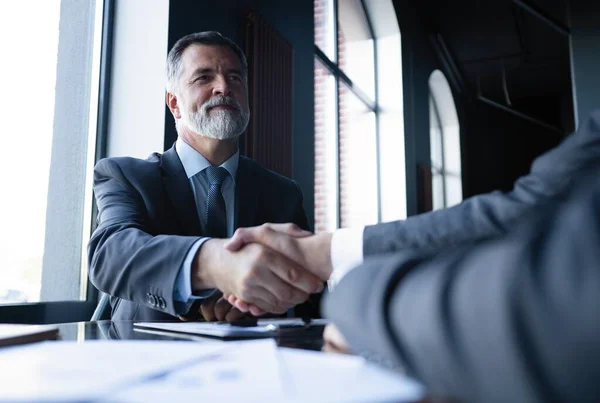 Καλή συμφωνία. Δύο επιχειρηματίες σφίγγουν το χέρι ενώ κάθονται στο χώρο εργασίας. — Φωτογραφία Αρχείου