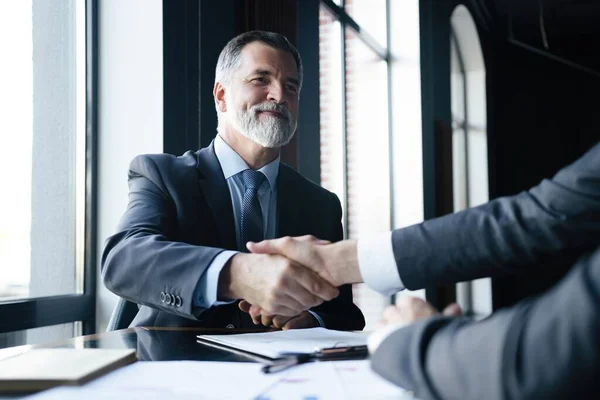 Bonne affaire. Deux hommes d'affaires serrant la main alors qu'ils étaient assis sur le lieu de travail. — Photo