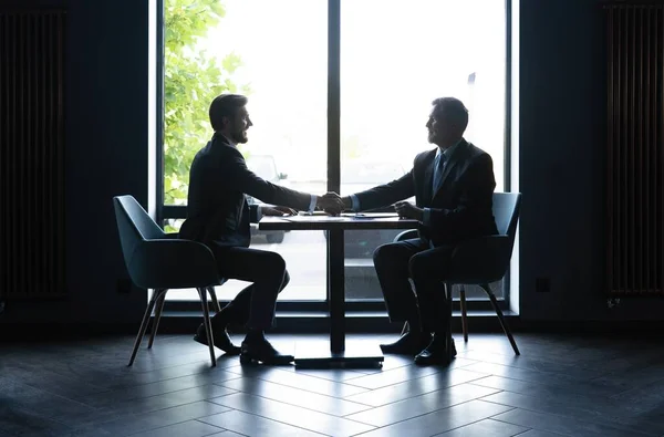 好交易。两个商人坐在工作场所握手. — 图库照片