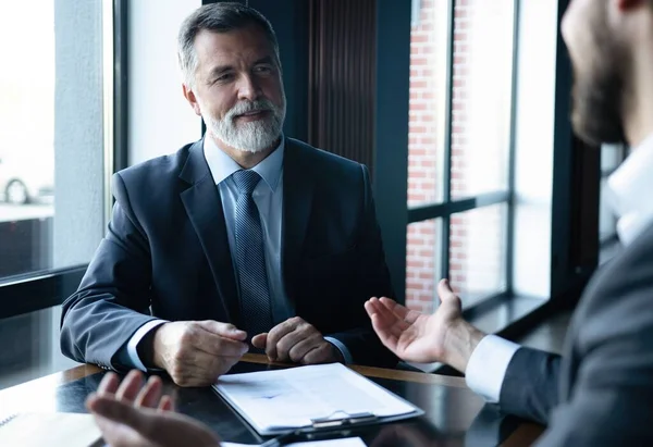 Senior en junior zakenman iets bespreken tijdens hun bijeenkomst, office achtergrond. Stockafbeelding